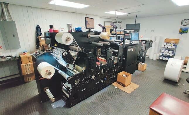 A printing machine in a room with a lot of rolls of paper.