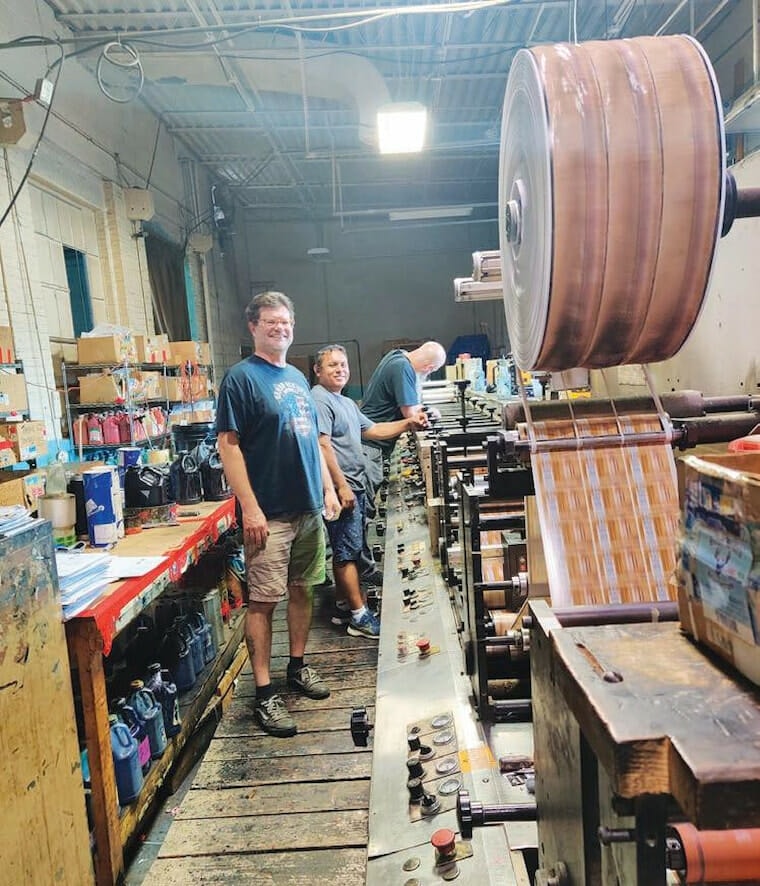 Two men standing in front of a label printing machine in a factory.